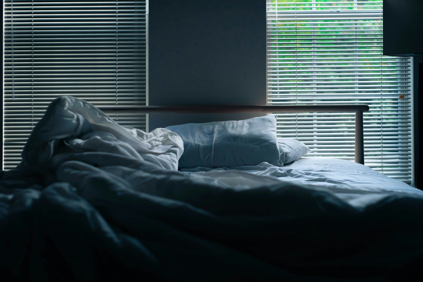 Chambre plongée dans la lumière bleue du soir, lit défait près d'un store