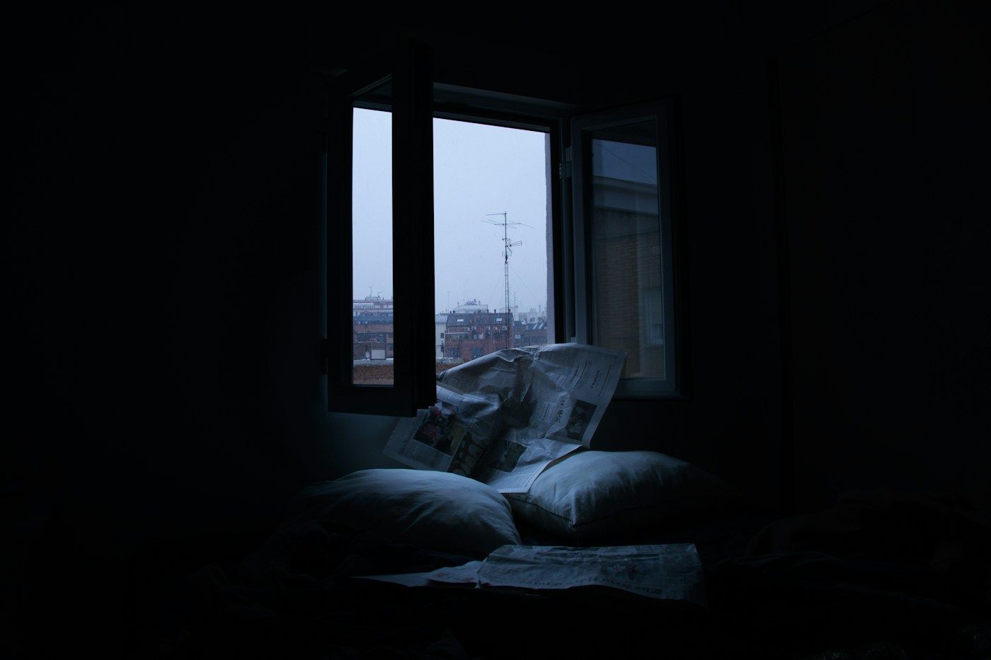 Fenêtre ouverte sur une ville éclairée, la nuit, depuis une chambre sombre
