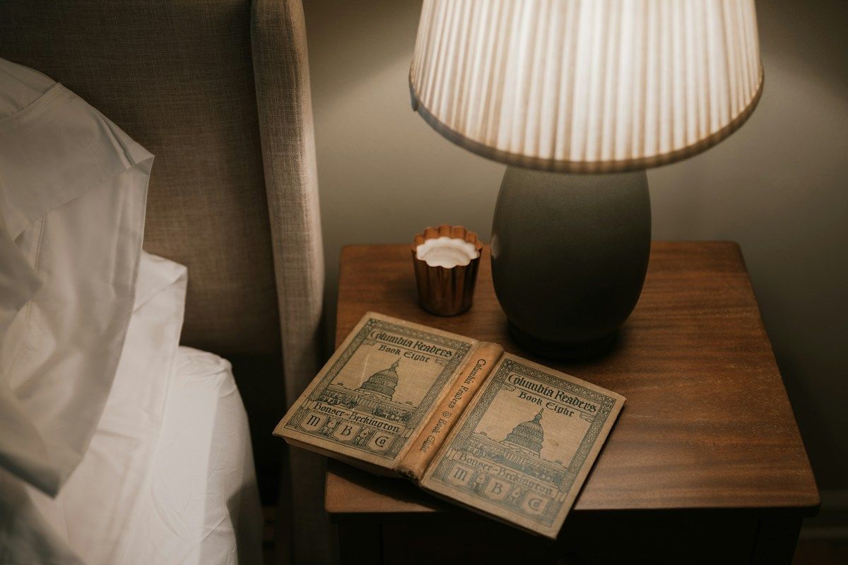 Livre ouvert sur une table de nuit, sous une lampe à l'abat-jour plissé