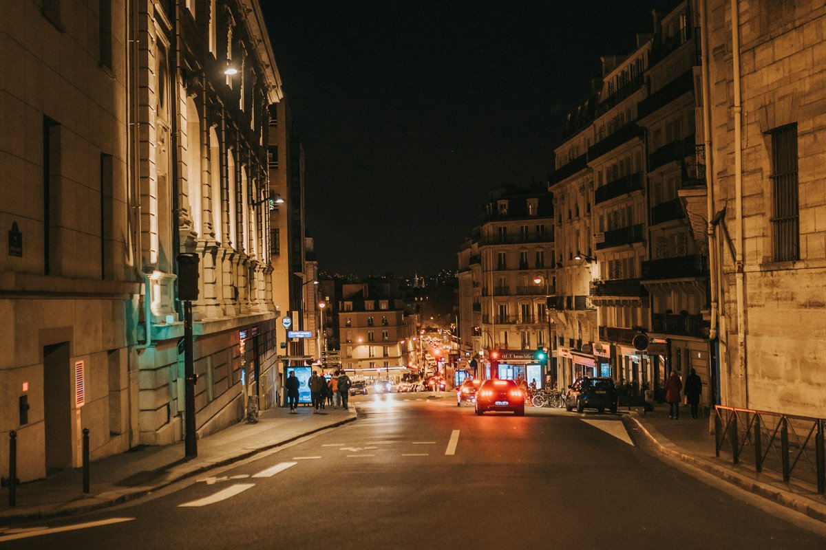 Rue d'une grande ville la nuit, façades éclairées par les réverbères et feux des voitures
