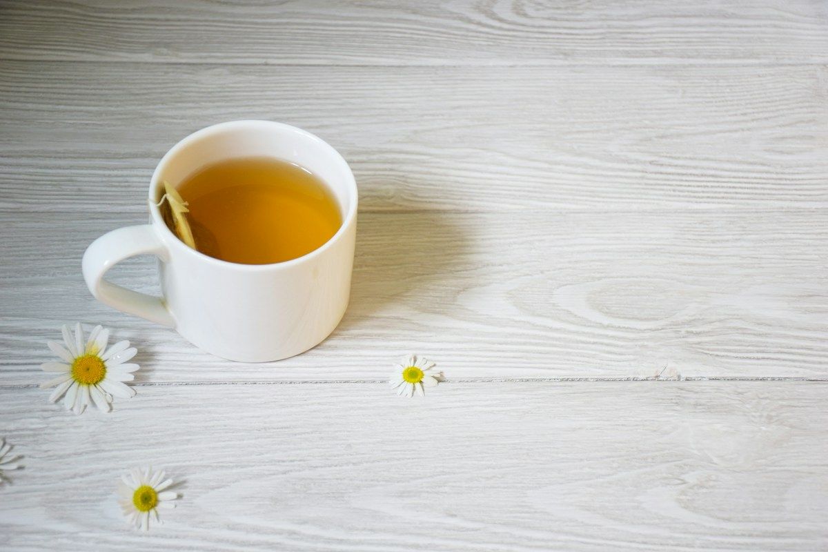 Tasse d'infusion et fleurs de camomille sur une table en bois blanc